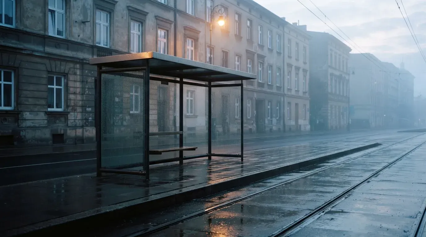 Pusta wiata przystanku tramwajowego na miejskiej ulicy o świcie, pusta ławka i mokry chodnik.