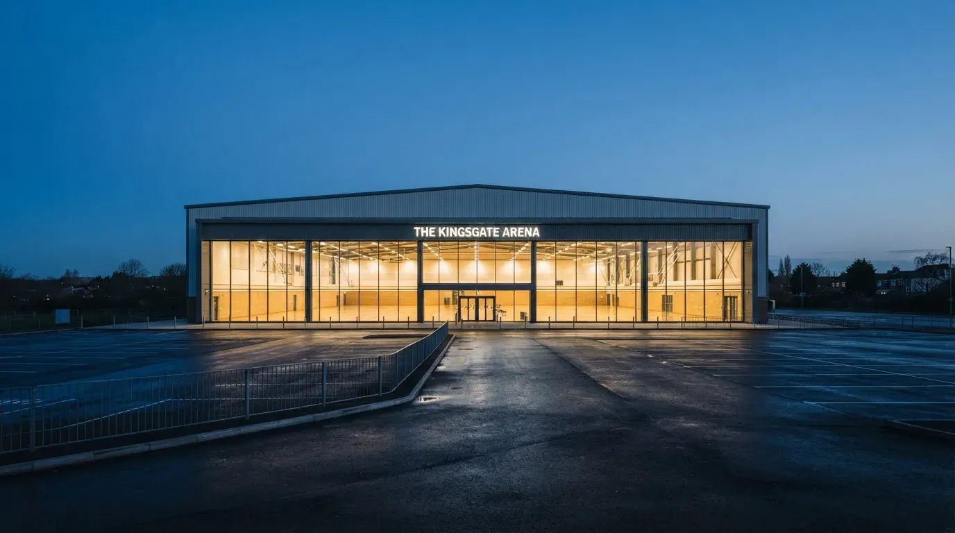 Duża hala sportowa widziana z daleka, parkiet jest pusty, a nad nim świecą rzędy reflektorów.