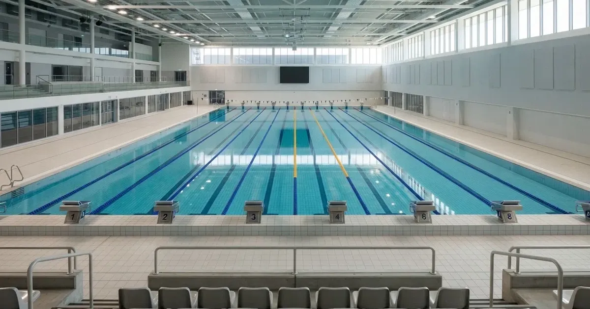 Pusty basen olimpijski z równymi torami i spokojną taflą wody, widok z trybun w jasnym świetle.